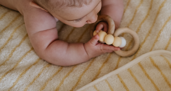 baby on a couch, playing with a toy, after body care with ATTITUDE products