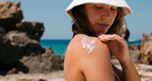 Woman on the beach applying sunscreen on her shoulder | ATTITUDE